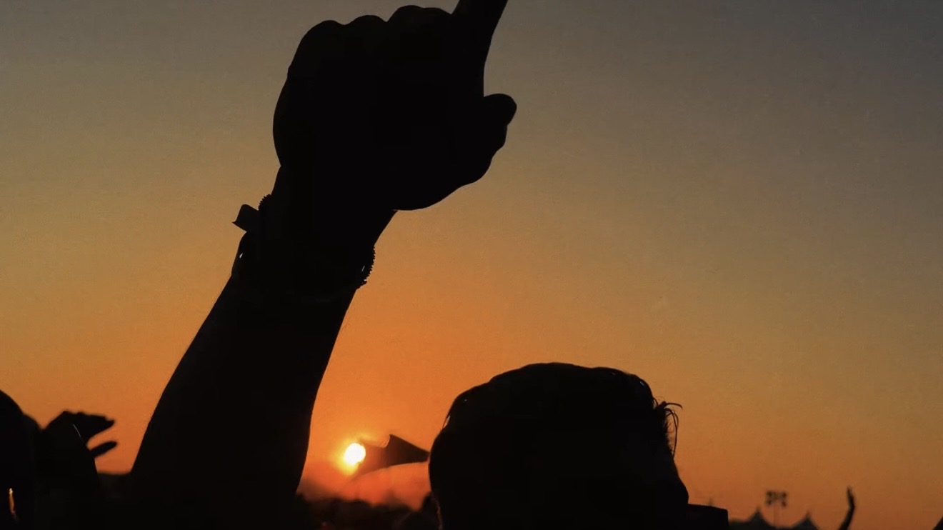 Crowd silhouettes with a raised hand against the setting sun at golden hour